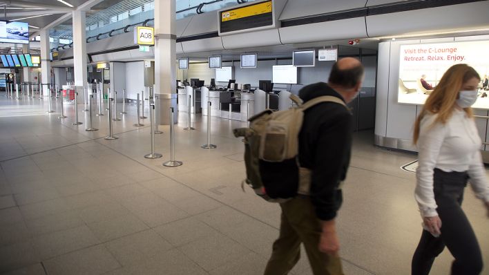 Mit Gesichtsmasken gehen zwei Passagiere an leeren Abfertigungsschaltern im Terminal des Flughafens Tegel vorbei. (Quelle: dpa/W. Kumm)