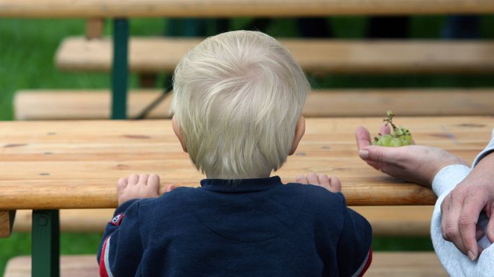 Ein kleiner Junge sitzt beim Sommerfest der Kinderhilfsorganisation Arche auf einer Bank. (Quelle: dpa/Stephanie Pilick)