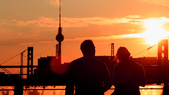 Symbolbild: Zwei Personen sitzen beim Sonnenuntergang auf der Modersohnbrücke in Berlin. (Quelle: dpa/M. Kusch)