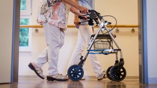Symbolbild: Eine Pflegekraft geht in einem Pflegeheim mit einer älteren Dame über einen Korridor. (Quelle: dpa/C. Schmidt)