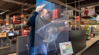 Ein Mitarbeiter installiert in einem Supermarkt eine Plexiglascheibe an der Kasse (Quelle: dpa/Robert Michael)