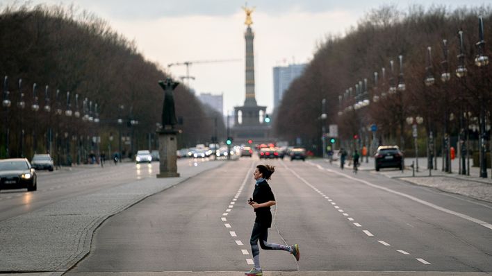 19.03.2020, Berlin: Eine Läuferin überquert die nahezu leere Straße des 17. Juni vor dem Brandenburger Tor (Quelle: dpa/Nietfeld)