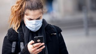 Eine Frau mit Mundschutz blickt auf dem Alexanderplatz auf ihr Smartphone (Bild: dpa/Kay Nietfeld)