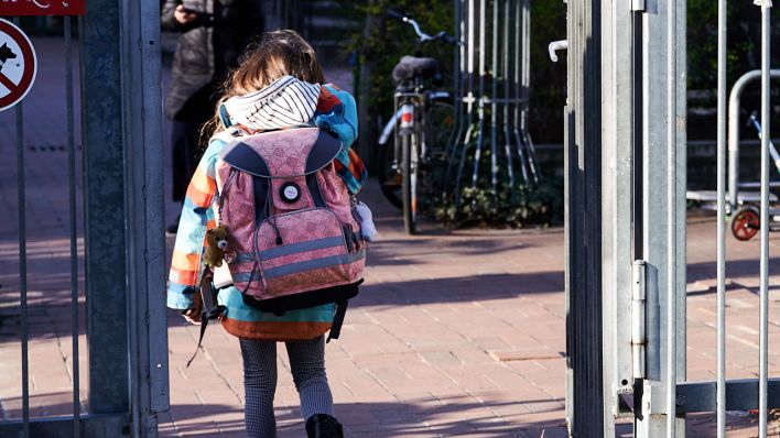 Ein Schulkind geht mit ihrem Schulranzen durch das Eingangstor einer Schule (Bild: dpa/Annette Riedl)