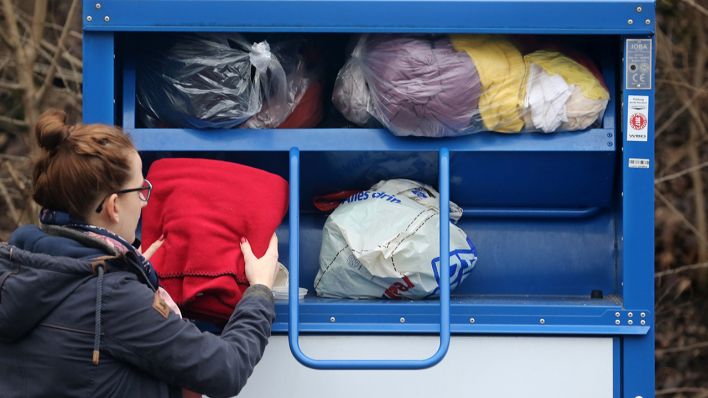Symbolbild: Eine Person entsorgt gebrauchte Textilien in einem Altkleidercontainer. (Quelle: dpa/Roland Weihrauch)