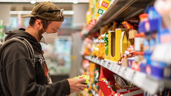 Ein Kunde steht in einem Supermarkt vor einem Regal, und trägt dabei einen Mundschutz. Quelle: Robert Michael/dpa