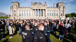 Polizeibeamte mit Mund-Nasen-Schutz stehen in einer Menschenmenge auf der Reichstagswiese vor dem Reichstagsgebäude. (Quelle: dpa/Kay Nietfeld)