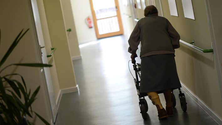 Eine alte Frau geht am 05.12.2012 in Berlin im Seniorenpflegeheim pro Vita Haus Rheingold mit einem Rollator einen Flur entlang. (Quelle: dpa/Jens Kalaene)