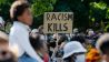 Ein Teilnehmer einer Kundgebung gegen den gewaltsamen Tod des Afroamerikaners George Floyd durch einen weißen Polizisten hält vor der US-Botschaft ein Plakat mit der Aufschrift „Racism kills“ (Rassismus tötet) hoch. (Quelle: dpa/C. Soeder)
