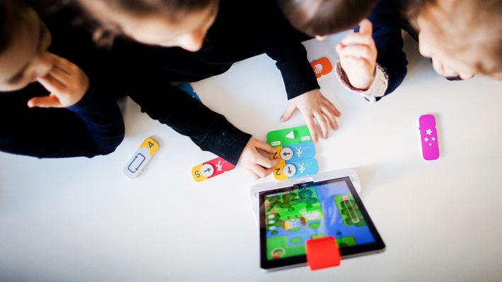 Kinder in einer Kindertagesstätte lernen spielerisch Coden. Die Kinder bewegen hier durch Programmierbefehle mit digitalen Bauklötzen ein Monster in einem Spiel auf dem iPad. (Quelle: dpa/Vennenbernd)