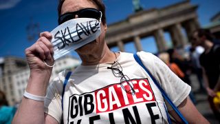 Eine Frau posiert bei einer so genannten Hygiene-Demo in Berlin vor dem Brandenburger Tor mit einem <<Gib Gates keine Chance>> T-Shirt bekleidet und legt eine Maske mit der Aufschrift <<Sklave>> ab. (Quelle: imago images/S. Boness)