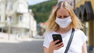 Eine Frau mit Mund-Nasen-Maske schaut auf ihr Smartphone. (Quelle: imago-images/HMB Media)