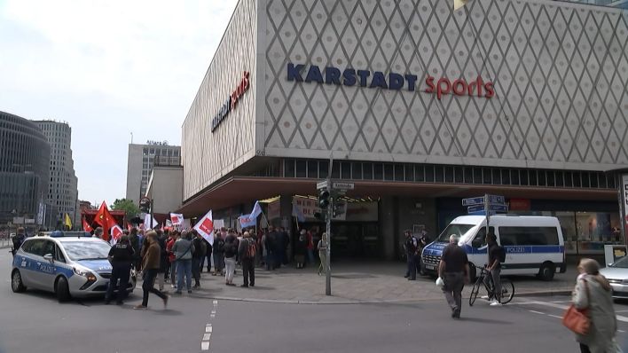 Menschen demonstrieren vor einer Karstadt Sports Filialie.