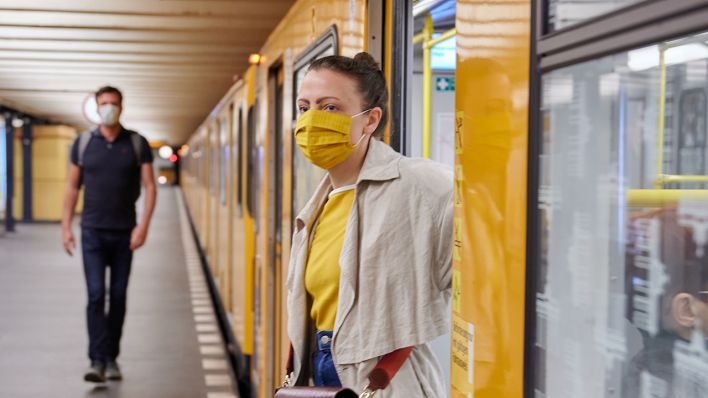 Eine Frau trägt einen Mund-Nasen-Schutz, als sie aus der U-Bahn am Rosa-Luxemburg Platz aussteigt