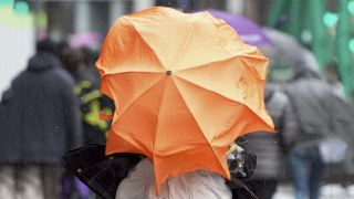 Von einer heftigen Windböe überrascht wird eine Frau mit Schirm (Quelle: dpa/Boris Roessler)