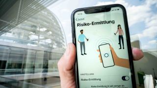 Die Corona-Warn-App mit der Seite zur Risiko-Ermittlung ist im Display eines Smartphone vor der Kuppel des Reichstags zu sehen (Bild: dpa/Michael Kappeler)