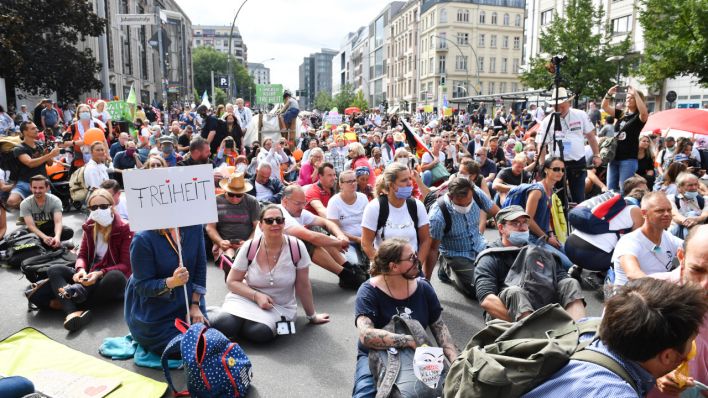 Teilnehmer sitzen auf der Straße bei einer Demonstration gegen die Corona-Maßnahmen. (Quelle: dpa/Bernd Von Jutrczenka)