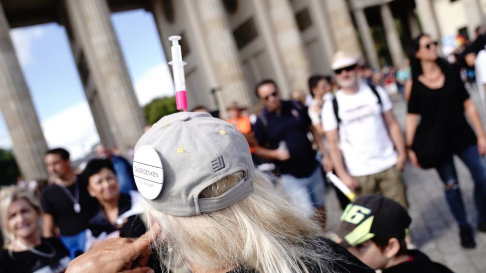 Ein Teilnehmer trägt eine Kappe mit einer Spritze und einem Button "Querdenken 711 Stuttgart" am Brandenburger Tor bei einer Demonstration gegen die Corona-Maßnahmen. (Quelle: dpa/Kay Nietfeld)