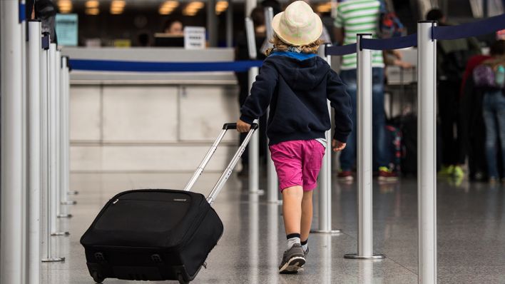 Ein Kind mit Strohhut zieht seinen Koffer im Terminal eines Flughafens. (Quelle: dpa/Andreas Arnold)