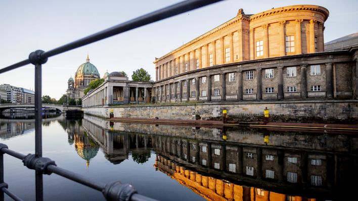 Die Alte Nationalgalerie (r) und der Berliner Dom (l) spiegeln sich im Licht der aufgehenden Sonne in der Spree. (Quelle: dpa/Christoph Soeder)
