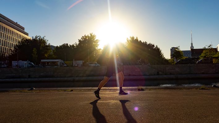 Nur die Beine eines Läufers sind im Regierungsviertel zu sehen, als er im Gegenlicht der Sonne entlang der Spree läuft. (Quelle: dpa/Paul Zinken)