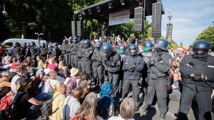 Polizisten stehen bei einer Kundgebung gegen die Corona-Beschränkungen auf der Straße des 17. Juni zwischen Teilnehmern vor einer Bühne. (Quelle: dpa/Christoph Soeder)