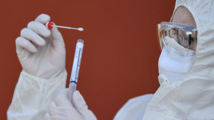 Eine Arzthelferin in Schutzausrüstung hält einen Abstrichtest auf das Coronavirus Sars-Cov-2 in ihren Händen. (Quelle: dpa/Patrick Pleul)