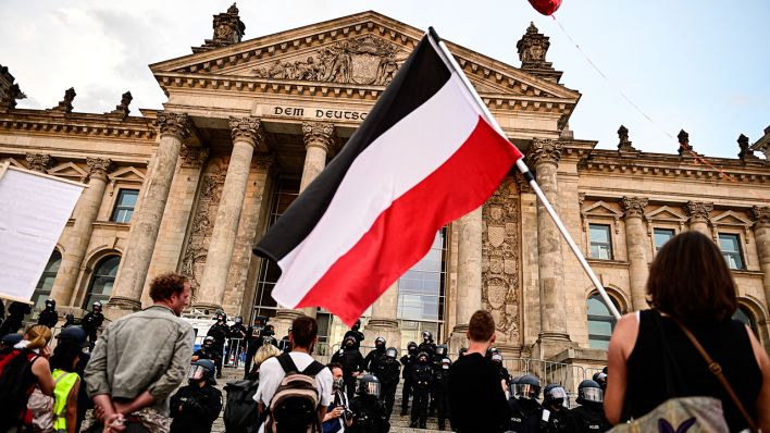 29.08.2020, Berlin: Teilnehmer einer Kundgebung gegen die Corona-Maßnahmen stehen vor dem Reichstag, ein Teilnehmer hält eine Reichsflagge (Quelle: dpa / Fabian Sommer).