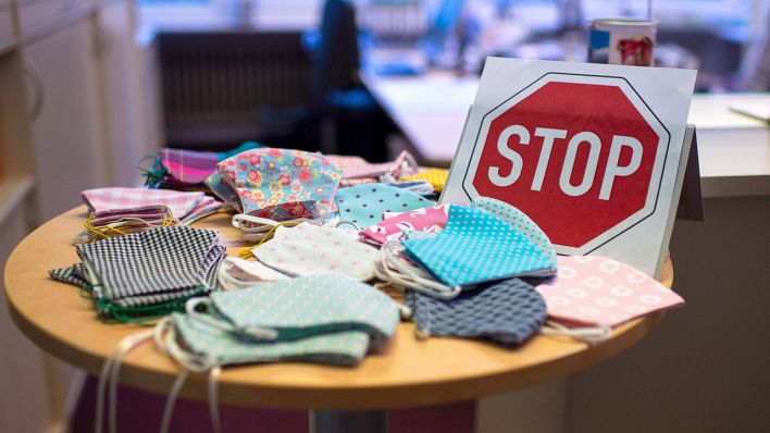 Symbolbild: Mundnsenschutz-Masken liegen auf einem Tisch vor einem aufgestellten Stop-Schild. (Quelle: imago images/N. Wedel)