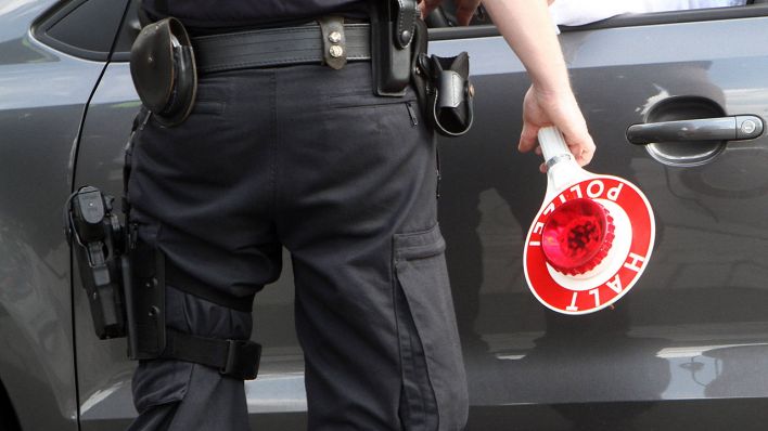 Polizist hält eine Stoppkelle in der Hand und kontrolliert eine Autofahrerin. Quelle: www.imago-images.de