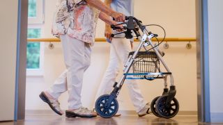 Eine Pflegekraft geht in einem Pflegeheim mit einer älteren Dame über einen Korridor. (Quelle: dpa/Christoph Schmidt)