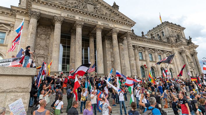 Teilnehmer einer Kundgebung gegen die Corona-Maßnahmen stehen auf den Stufen zum Reichstagsgebäude, zahlreiche Reichsflaggen sind zu sehen. Foto: Achille Abboud/NurPhoto/dpa