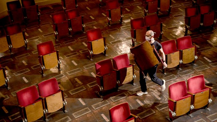 Ein Mitarbeiter trägt Stühle aus den Sitzreihen des Zuschauerraums des Berliner Ensembles. (Quelle: dpa/Britta Pedersen)