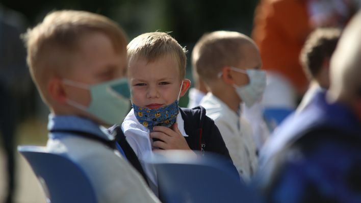 Symbolbild: Schüler sitzen mit Mund-Nasenschutz vor der Einschulungsfeier vor dem Schulgebäude. (Quelle: dpa/Matthias Bein)