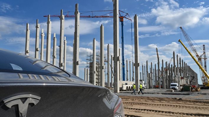 Ein Elektrofahrzeug der Marke Tesla steht vor einem Rohbau auf der Baustelle der Tesla Gigafactory. (Quelle: dpa/Patrick Pleul)