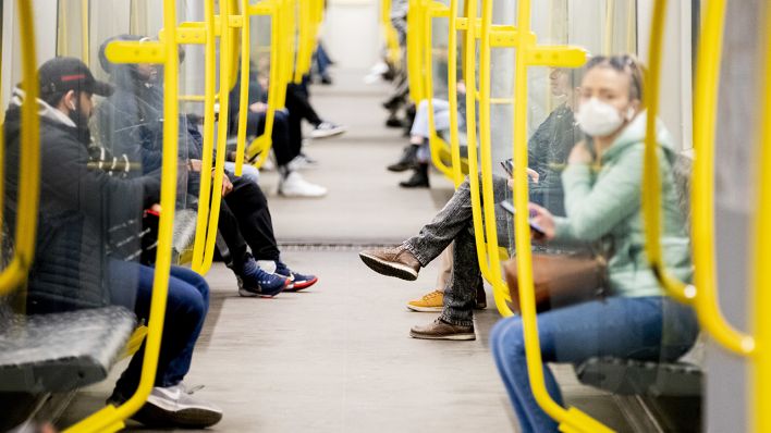 Fahrgäste sitzen in einer U-Bahn, wobei eine Frau einen Mundschutz trägt. Quelle: dpa