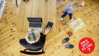 Eine Frau sitzt zu Hause am Schreibtisch und arbeitet. Neben ihr spielt ein Kind. (Quelle: imago-images/Thomas Trutschel)