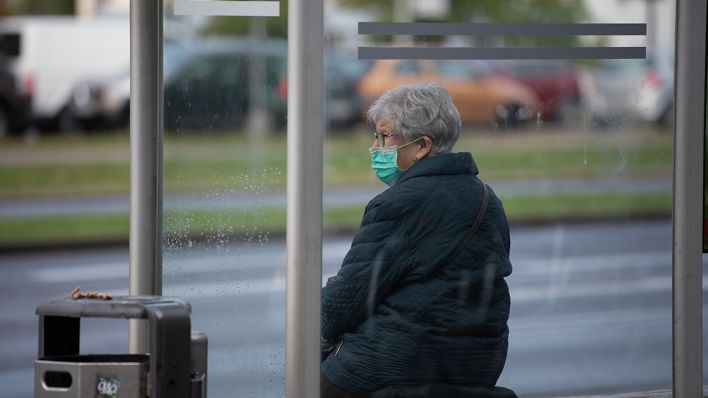 Eine Frau mit Mund- und Nasenschutz sitzt am 12.10.2020 an einer Haltestelle in Cottbus. (Quelle: dpa/Paul Zinken)