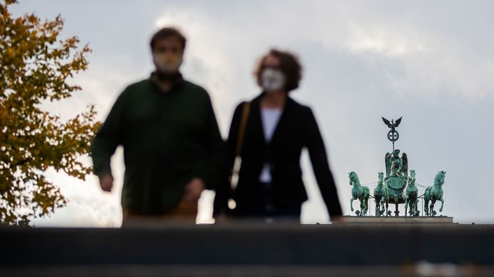 Ein Mann und eine Frau mit Mund-Nasen-Schutz gehen am 24.10.2020 vor der Quadriga des Brandenburger Tores. (Quelle: dpa/Christoph Soeder)