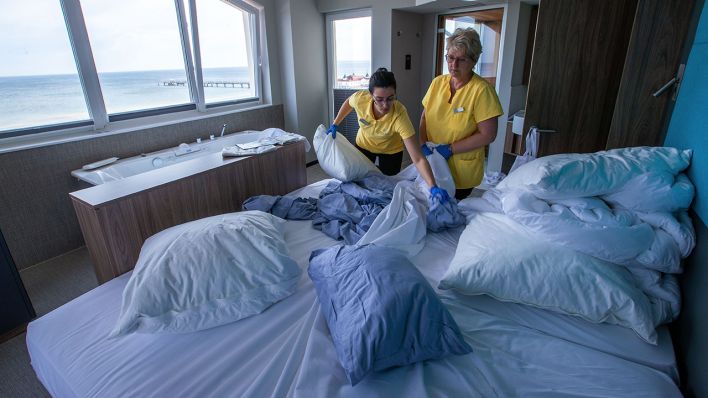 Zwei Hotelmitarbeiterinnen ziehen die Wäsche von einem Gästebett ab. (Quelle: dpa/Jens Büttner)