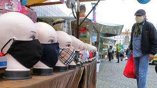 Eine Person, die einen Mund-Nasen-Schutz trägt, betrachtet auf einem Wochenmarkt auf dem Hermannplatz im Bezirk Neukölln handgefertigte Schutzmasken, die zum Kauf angeboten werden. (Quelle: dpa/Wolfgang Kumm)