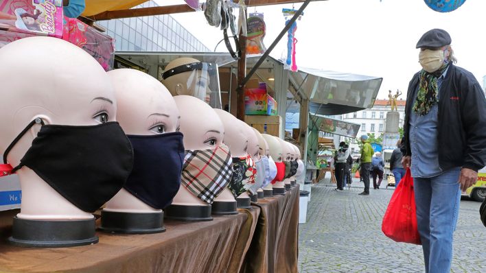 Eine Person, die einen Mund-Nasen-Schutz trägt, betrachtet auf einem Wochenmarkt auf dem Hermannplatz im Bezirk Neukölln handgefertigte Schutzmasken, die zum Kauf angeboten werden. (Quelle: dpa/Wolfgang Kumm)