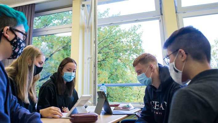 Symbolbild: SchülerInnen sitzen in einem Klassenzimmer bei geöffnetem Fenster mit Mund-Nase-Schutzmasken. (Quelle: dpa/D. Bockwoldt)