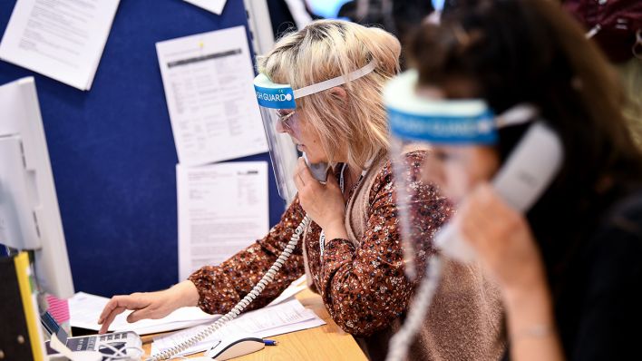 Berlin: Mitarbeiter des Gesundheitsamtes Mitte mit Gesichtsschutzschirm telefonieren im Lagezentrum des Gesundheitsamt Mitte. Quelle: dpa/Britta Pedersen