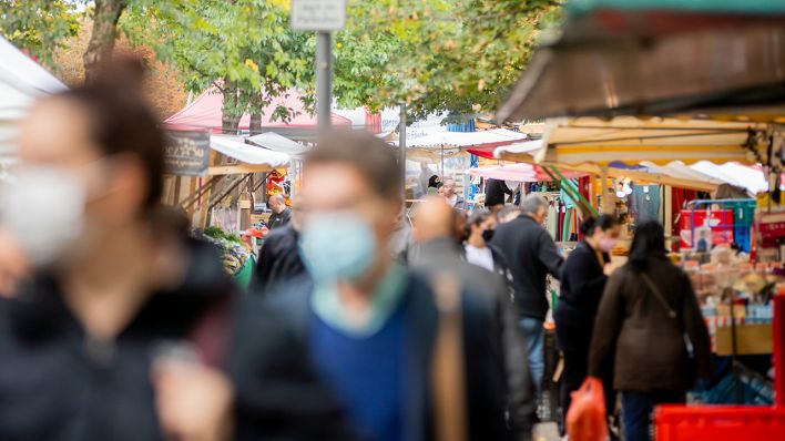 Menschen tragen Mund-Nasen-Bedeckungen und gehen in Berlin-Kreuzberg über den Markt am Maybachufer. Foto: Christoph Soeder/dpa