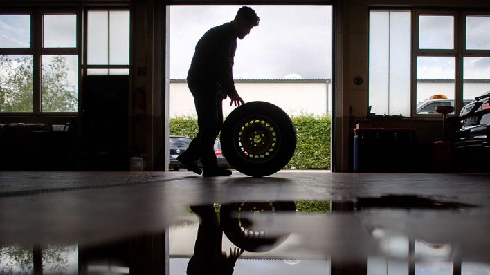 Symbolbild: fZ-Mechatroniker rollt einen Reifen durch eine Werkstatt (Quelle: dpa/Julian Stratenschulte)