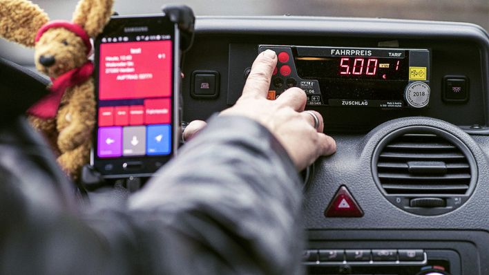 Ein Taxifahrer drückt einen Knopf auf seinem Taxameter (Bild: imago images/Björn Hake)