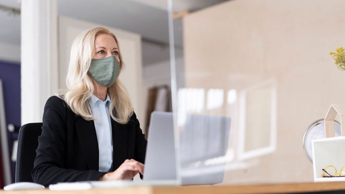 Symbolbild: Eine Frau sitzt in einem Büro und trägt dabei eine Nase-Mund-Schutzmaske. (Quelle: imago images/R. Page)
