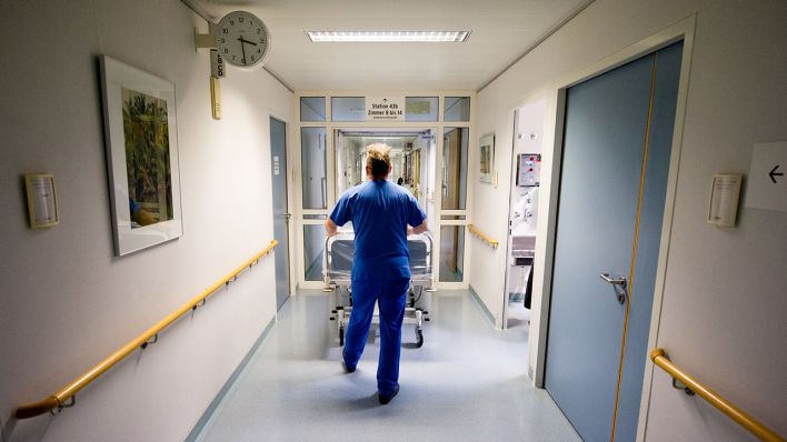 Symbolbild - Ein Krankenpfleger schiebt in einer Klinik ein Krankenbett durch den Flur. (Bild: dpa/Daniel Bockwoldt)