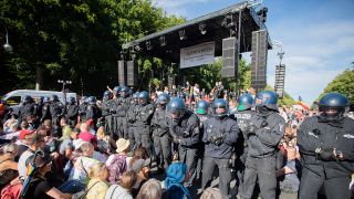 Archiv- Polizisten stehen am 01.08.2020 bei einer Kundgebung gegen die Corona-Beschränkungen auf der Straße des 17. Juni zwischen Teilnehmern vor einer Bühne. (Bild: dpa/Christoph Soeder)